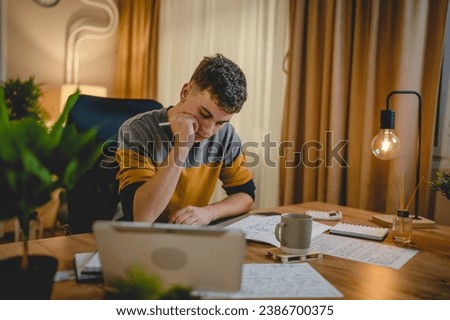 Young caucasian man teenager student study at home at the table at night or evening determinate learning prepare lesson or exam alone real people copy space Royalty-Free Stock Photo #2386700375