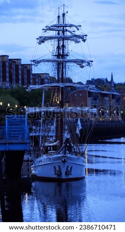 A majestic tall sailing ship is pictured on the banks of the River Tyne, with the river and surrounding cityscape providing an idyllic backdrop