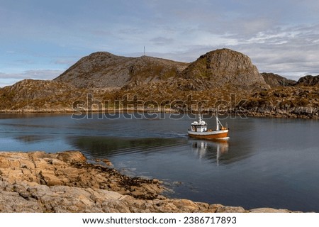 A sailboat is pictured on a body of water, surrounded by mountainous terrain and jagged rocks