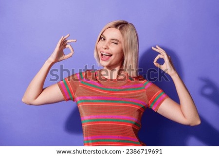 Photo portrait of young funky smiling girl in red striped t shirt blink eye approve your test results isolated on violet color background
