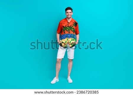 Full size photo of satisfied pleasant guy wear tropical shirt stylish shorts standing arms in pockets isolated on blue color background