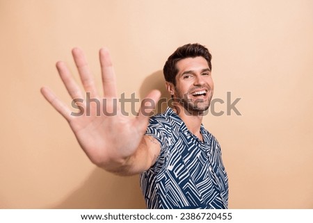 Portrait of good mood pleasant guy with trendy hairdo wear stylish shirt waving palm to you say hi isolated on beige color background