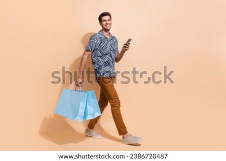 Full length photo of walking businessman carry brand new clothes shopaholic hold phone got promocode isolated on beige color background Royalty-Free Stock Photo #2386720487