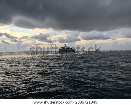 A stunning sunset over a tranquil ocean, with clouds in the sky and small boats in the background
