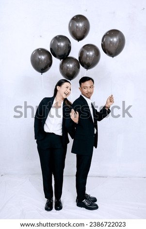 Portrait of a happy couple taking pre-wedding photos in the studio using props or holding black balloons. isolated on white background.