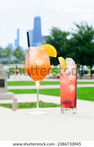 Two colorful cocktails with garnishes on an outdoor table with a city skyline in the background Royalty-Free Stock Photo #2386733045