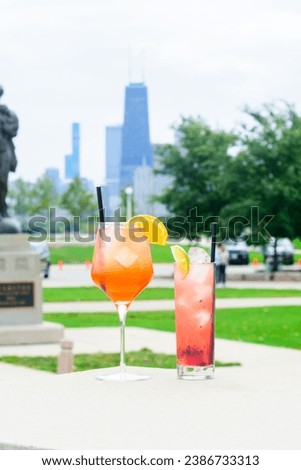 Two colorful cocktails with garnishes on an outdoor table with a city skyline in the background Royalty-Free Stock Photo #2386733313
