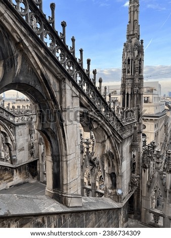 Duomo, Italy, Ornate Gothic arches and spires of a cathedral rooftop, showcasing elaborate stonework against a cityscape backdrop.