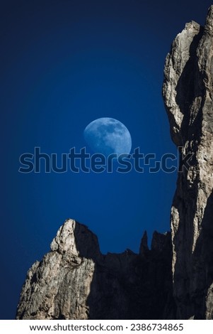 A full moon is seen in the sky above some rocks