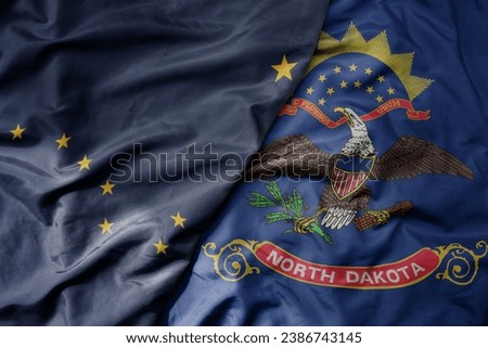 big waving colorful national flag of north dakota state and flag of alaska state . macro