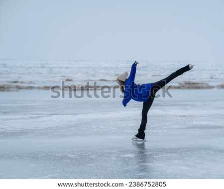 Caucasian woman in a blue sweater is skating on a frozen lake. Figure skater performs a swallow. 
