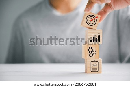 Hand grasping a wooden block cube with an icon, emphasizing the importance of company strategy development. Success and business goals depicted.