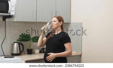 Pensive pregnant woman drinking water in the kitchen. Young happy expectant thinking about her baby and enjoying her future life. Motherhood, pregnancy
