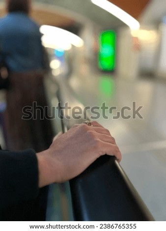 Woman's hand on a moving walkway, vertical shot capturing the essence of routine airport travel. Copyspace available. Royalty-Free Stock Photo #2386765355