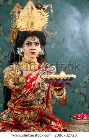 Portrait of beautiful Indian girl of Durga Idol Agomoni Concept Indoor Photo wearing traditional Indian saree, gold jewellery, and bangles. Maa Durga agomoni shoot concept.Indian culture durga puja.