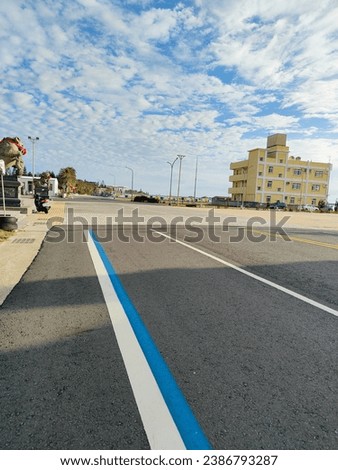 White and blue lines on the side of the road in Suogang, Penghu, Taiwan that stretch with blue sky and white clouds. Picture taken in the morning when the sun shines brightly in Suogang Harbor, Taiwan