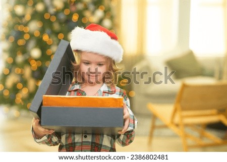 Kid boy in santa hat near christmas tree at home.