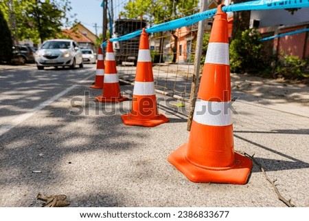 Several orange traffic cones with white fluorescent stripes are on the road for pointing to alert and divert traffic, sign with boundary are symbols of caution.