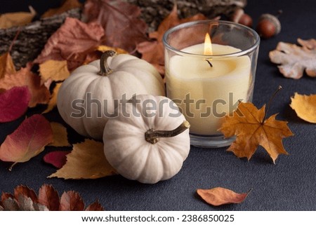 Small decorative pumpkins and glass aroma candle as cozy home decor on dark background for Fall and Thanksgiving holidays