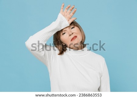 Elderly tired sick ill sad exhausted woman 50s wearing white knitted sweater put hand on forehead suffer from headache isolated on plain blue color background studio portrait. People lifestyle concept