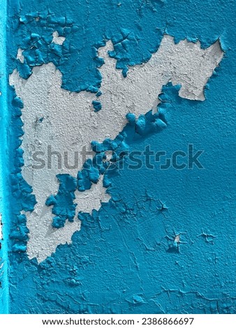 Peeling of the blue painted walls, white cement and time-worn paint are visible in the center of the picture behind the blue paint on the walls.