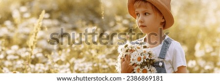 Portrait of a girl in a hat and denim overalls with a bouquet of daisies in a field. Concept of happiness, innocence, childhood or summer. Banner with copy space.