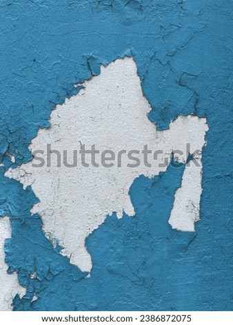 Peeling of the blue painted walls, white cement and time-worn paint are visible in the center of the picture behind the blue paint on the walls.