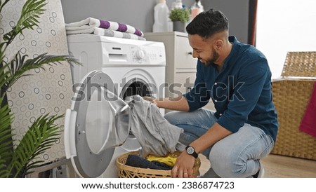 Young hispanic man doing laundry with washing machine at laundry room Royalty-Free Stock Photo #2386874723