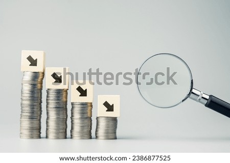 Decreasing arrow graph on lower fewer coins heaps with magnifying glass, economic recession analysis, less income, and savings, business in decline period Royalty-Free Stock Photo #2386877525