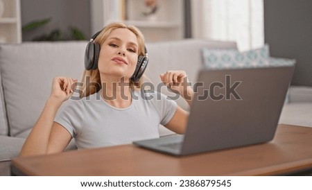 Young blonde woman listening to music and dancing sitting on floor at home