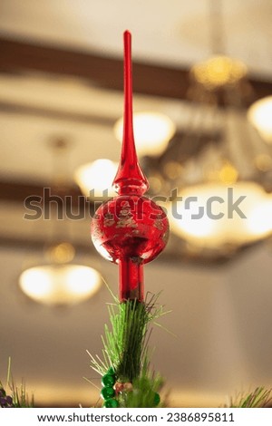 Red glass top on a Christmas tree close-up. Defocused chandelier in the background


