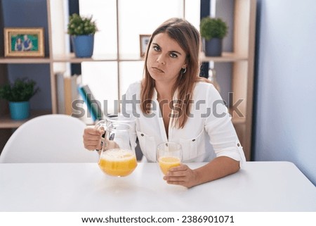 Young hispanic woman drinking glass of orange juice depressed and worry for distress, crying angry and afraid. sad expression.  Royalty-Free Stock Photo #2386901071