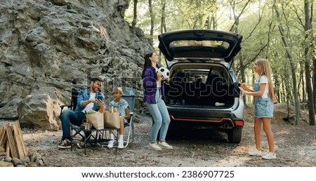 Mother and daugher in nature playing ball in forest near car. Father and son using phone and smiling talking during family vacation in nature. Child fun with mother father park. Family road trip with