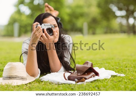 Brunette lying on grass taking picture in the park