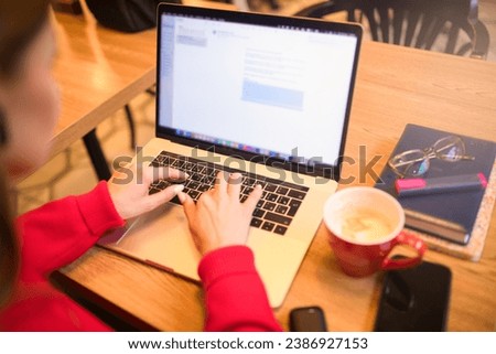 Woman experience web content writer keyboarding on laptop computer while sitting in restaurant with cup of coffee. Focus on hands and notebook gadget 