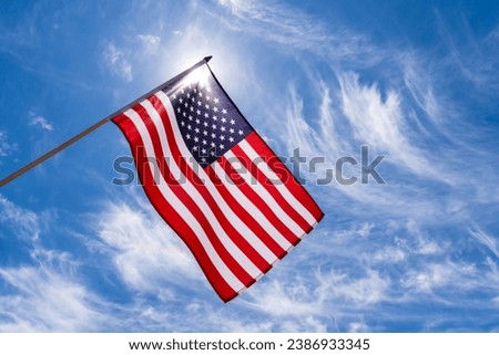 American flag waving in a blue sky with streaked clouds background. The national red, white and blue star striped USA, United States flag flying high is a patriotic symbol of freedom, honor and pride.