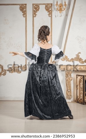 Beautiful woman in black rococo style medieval dress standing near wall back pose Royalty-Free Stock Photo #2386952953