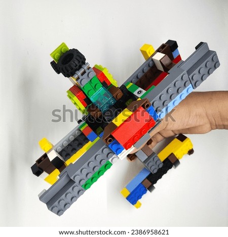 a picture of a toy airplane made from colorful squares of plastic, on the side of the airplane there is a boy's hand holding the airplane. with a pure white background