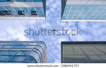Bottom view of modern office buildings group in downtown city with plane flying on white cloudy sky background