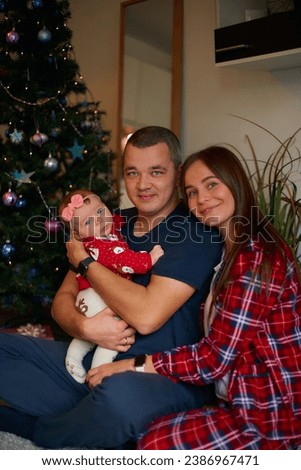 happy family consisting of mother, father and daughter having fun on the eve of Christmas near the Christmas tree in plaid pajamas in the comfort of home