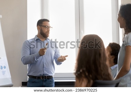 Serious confident busy project leader talking to employees on team meeting. Business coach, mentor teaching students, interns, explaining work tasks. Businessman presenting project to colleagues