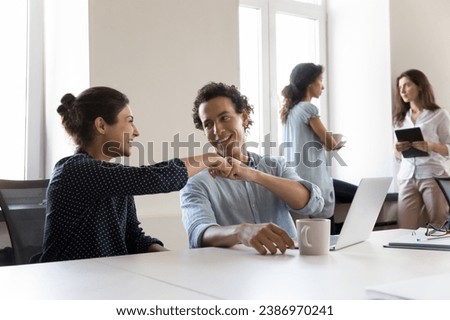 Two cheerful office friends celebrating business task completion, successful project startup, job promotion, sitting at shared workplace, giving fist bumps, talking, smiling, laughing Royalty-Free Stock Photo #2386970241