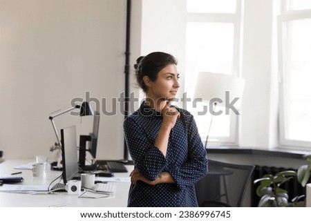 Calm thoughtful beautiful Indian young businesswoman in casual office portrait. Female manager, professional woman looking away with arms folded, touching chin, dreaming, thinking
