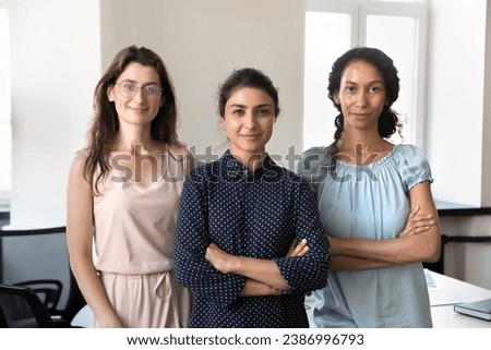 Happy confident beautiful diverse businesswomen standing together in office, looking at camera, smiling. Successful young business professionals women, leaders, colleagues front portrait