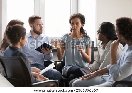 Serious African American group leader woman speaking on therapy meeting. Business team sitting on chairs in circle, talking, discussing solutions, project ideas, brainstorming