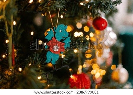 A New Year's toy in the shape of a green wooden dragon hangs on a branch on a Christmas tree. Glowing festive background. Chinese horoscope 2024. Zodiac sign Royalty-Free Stock Photo #2386999081
