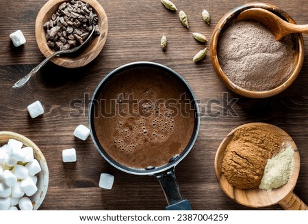 A look into a small pot of hot cocoa with ingredients all around to make it.