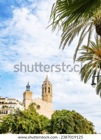 Church of St. Bartholomew and Santa Tecla in Sitges, Catalonia, Spain against a background of blue sky, palm trees and plants, vertical photo with copy space