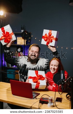 Christmas stream or video blog. Cheerful presenters in holiday clothes raffle off gifts for their subscribers. Male and female bloggers in New Year's outfits in a home studio.