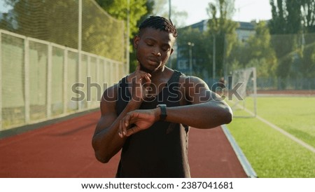 African American man runner jogger athlete muscular sportsman training outdoors athletic ethnic guy using smart band checking neck pulse heart rate result on smartwatch before running on sport stadium Royalty-Free Stock Photo #2387041681
